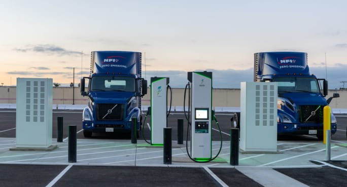 Blue NFI Volvo VNR electric trucks at electric charging stations