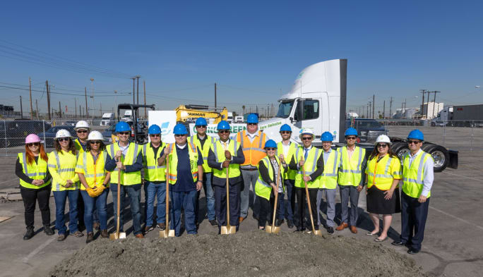 A line of people in yellow safety vests with shovels with an electric truck in the background, breaking ground on EV charging at the Port of Long Beach.