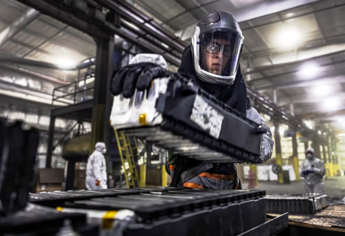 A technician in safety equipment is engaged in recycling work on a battery, ensuring safety and precision.