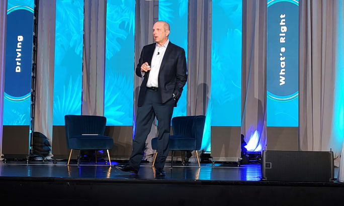 Man in business attire walks and talks on a stage.