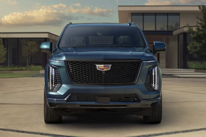 Sunny outdoor shot of a blue 2025 Cadillac Escalade SUV in the drive way of a house.