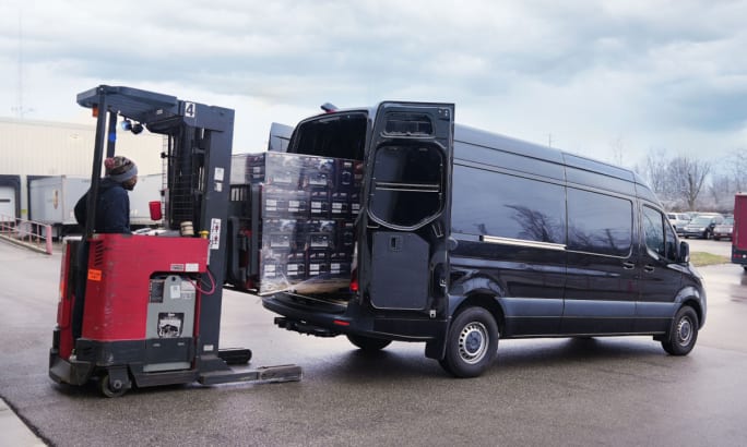 Forklift loading cargo into a Sprinter van through rear door.