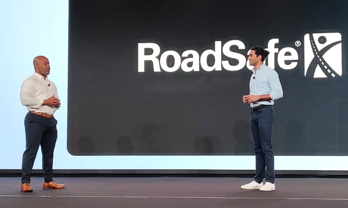 Two business men talk on a stage with a backdrop with logo for RoadSafe.