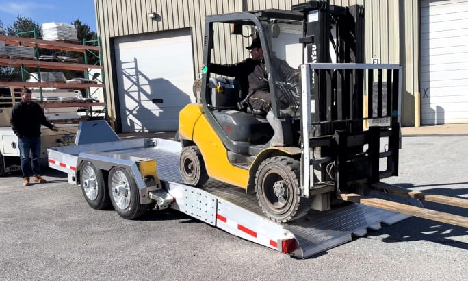 A Fork lift drives off a kneeling trailer.