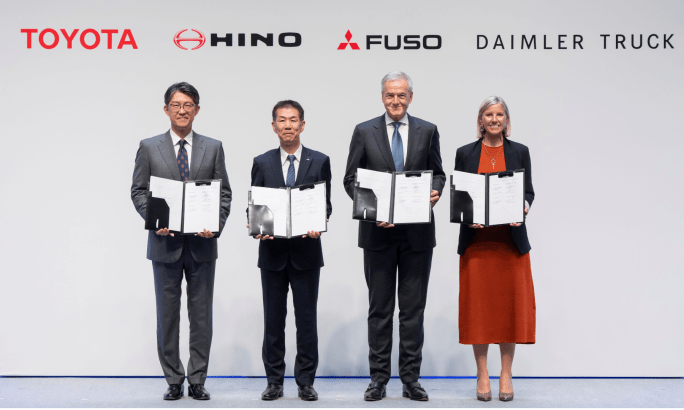 Three men and one woman in business attire on a stage holding documents.