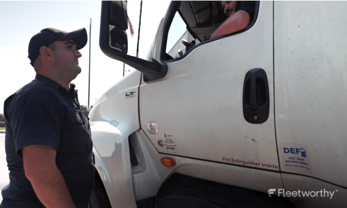 Motor vehicle inspection officer standing outside truck cab while talking to driver.