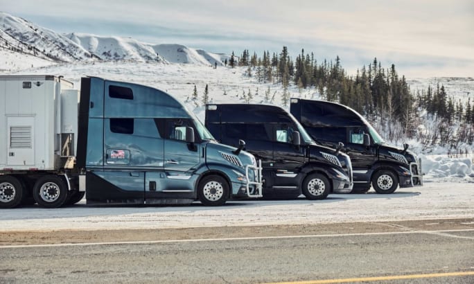 Three Volvo VNL trucks are parked side by side in a snowy landscape during cold weather testing, with pine trees and snow-covered hills in the background.