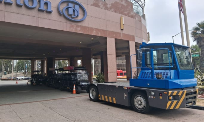 Side view of a blue ZM Trucks T75 electric terminal tractor parked near the Hilton hotel entrance.