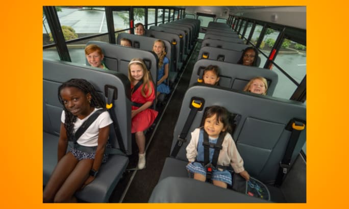 Group of schoolchildren seated on a bus, some using seat belts and child restraints, demonstrating safe school bus transportation.