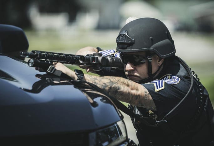 Tactical police officer aiming rifle from vehicle