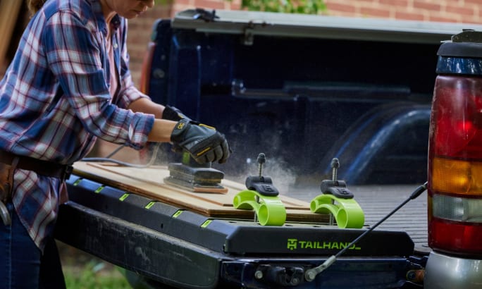 Worker cutting wood on a pickup tailgate.