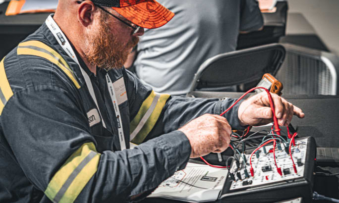 Technician using diagnostic tools to test truck electrical circuits at Top Tech 2025 competition.