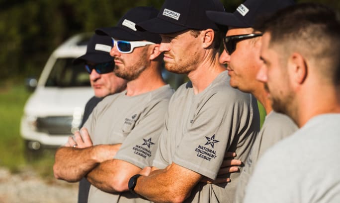 Close-up of competitors in National Equipment League shirts and hats during an event briefing.
