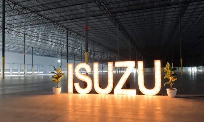 Illuminated Isuzu sign inside a large industrial building that is empty.