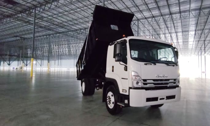 A white Isuzu dump bed truck parked inside a large industrial building.