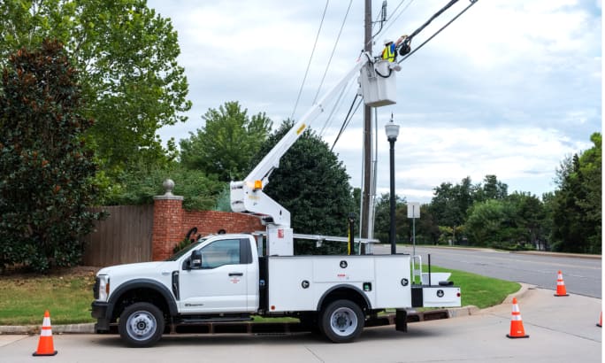 A bucket truck extended and a worker repairing utility lines.