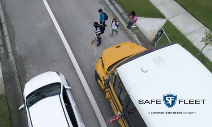 Overhead view of a school bus and children crossing the street as a car drives past.
