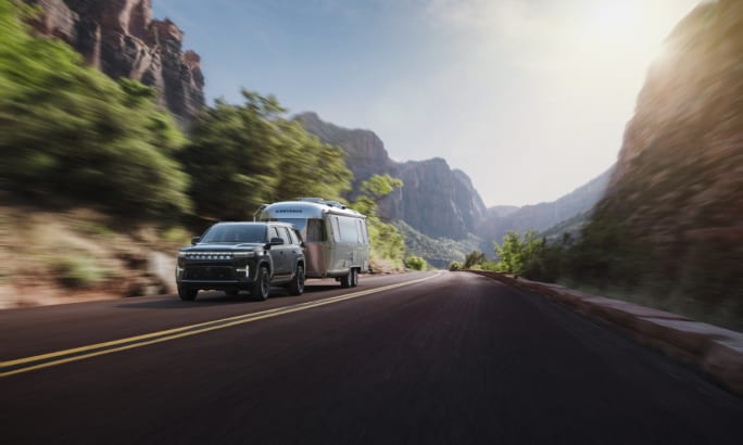 2026 Jeep Grand Wagoneer towing an Airstream trailer along a mountain highway.