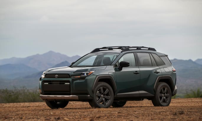Dark green 2026 Toyota RAV4 Woodland grade SUV parked on a dirt trail with mountains in the background.