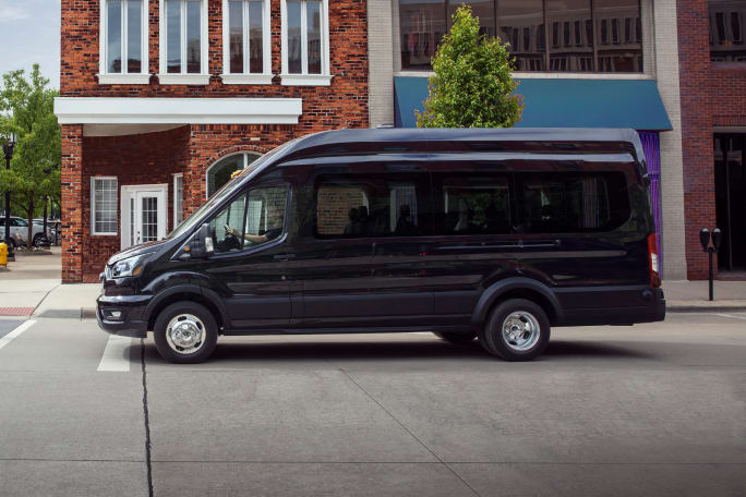 Side view of a 2026 Ford Transit Passenger Van driving in an urban area. Image highlights the updated model’s safety tech, software upgrades and configuration options for passenger and shuttle fleets.