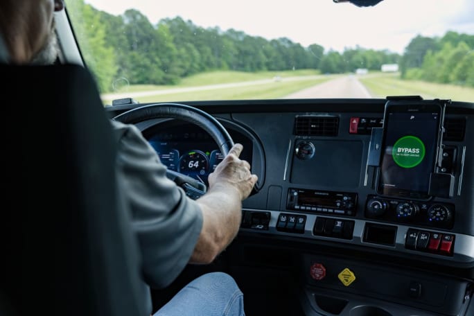 Driver in heavy-duty truck cab with a weigh station bypass notification on a tablet on the dashboard.