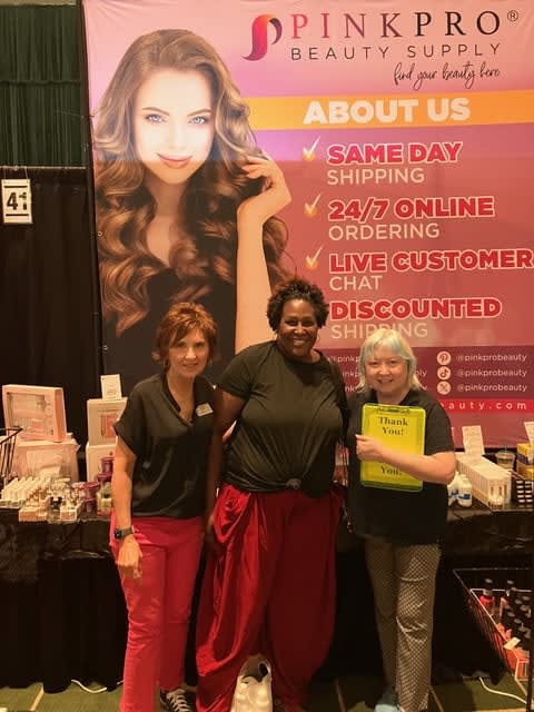 Three women stand in front of a banner advertising nail products