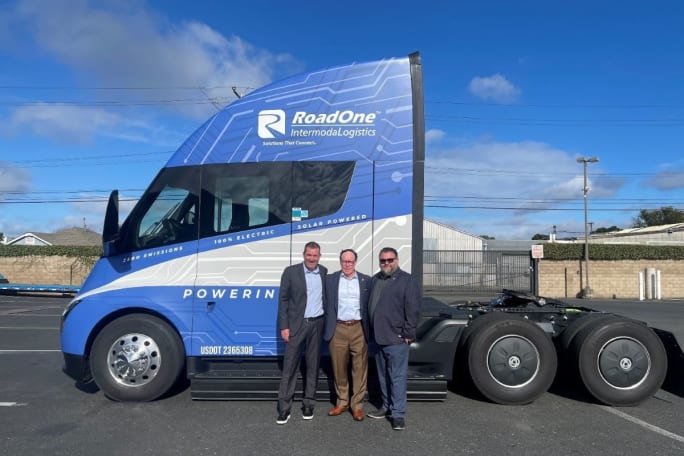 Blue Tesla Semi with RoadOne employees standing beside it