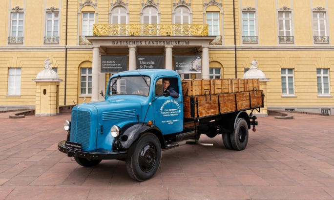 Blue vintage Mercedes-Benz flatbed truck parked in front of a historic museum building.