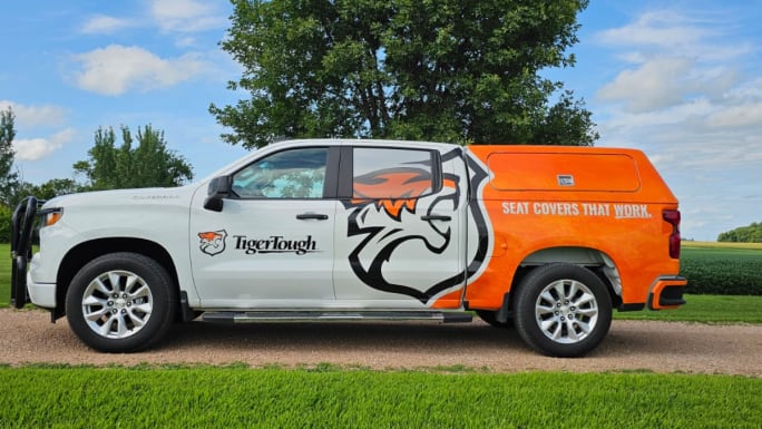 Tiger Tough branded pickup truck with orange and white wrap and tiger logo, parked outdoors, displaying the slogan “Seat Covers That Work.”