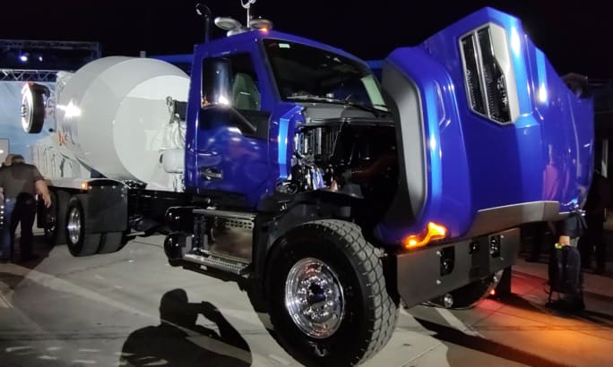 Blue concrete truck parked with the hood tipped open.