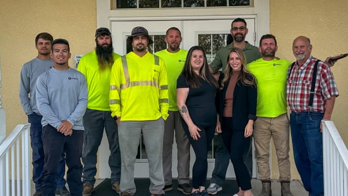 Group of Atwell employees pose together outside an office entrance, wearing a mix of work gear and casual clothing.