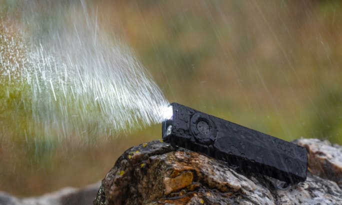 Flat style flashlight sitting on a rock with light comming out while in a heavy raind.