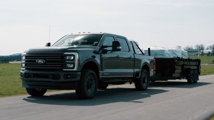 2027 Ford Super Duty pickup towing a trailer on a rural road during daylight.