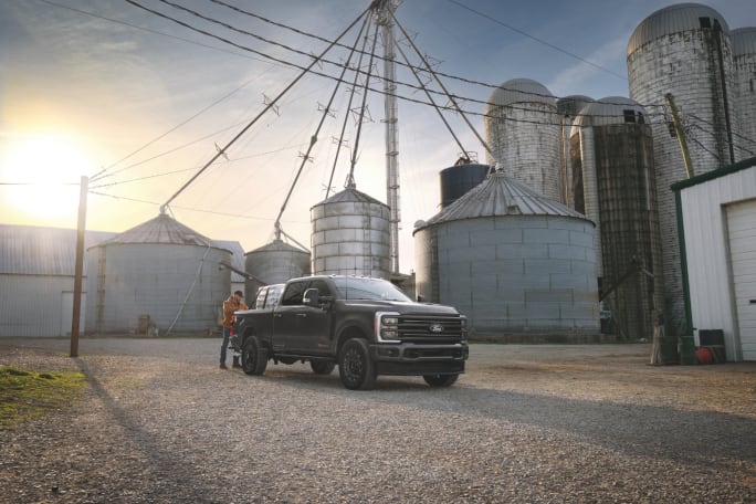 Ford Super Duty Carhartt edition parked on a farm near grain silos at sunset with a person standing beside the truck.