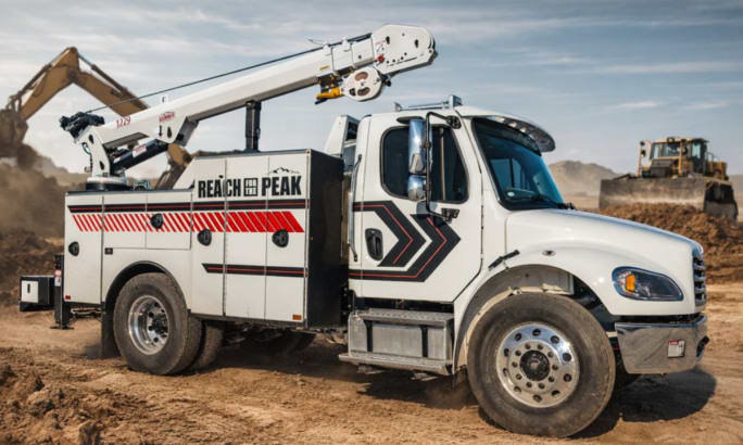 White heavy-duty truck with a service crane parked on a dirt job site. 