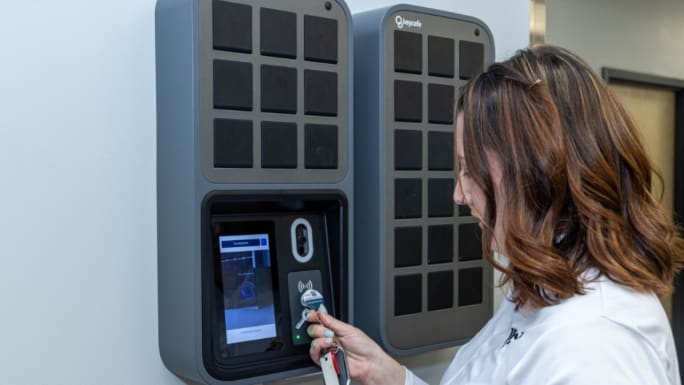 A woman holds a vehicle key fob to a Keycafe electronic key cabinet while accessing a stored fleet key.