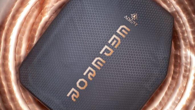 Close-up of an Adept Armor Emperor protective plate featuring a dark hexagonal-textured surface and prominent Emperor branding, displayed against a metallic copper-colored background.