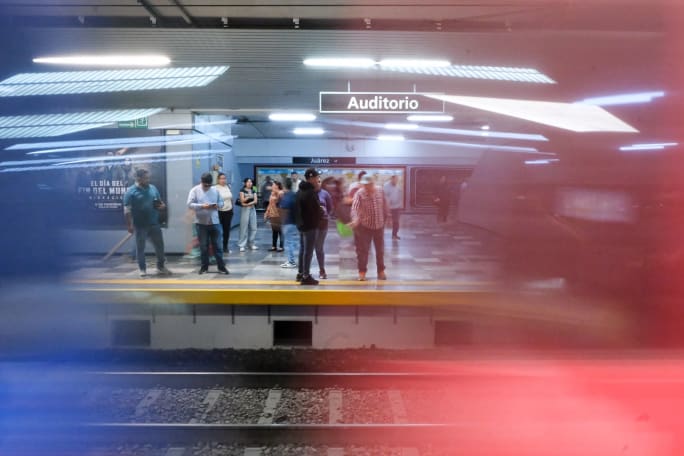 Rail patrons standing on a platform with red and blue colors in the foreground.