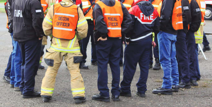 Group of emergency response personnel gathered in safety vests during a disaster briefing or response coordination meeting.