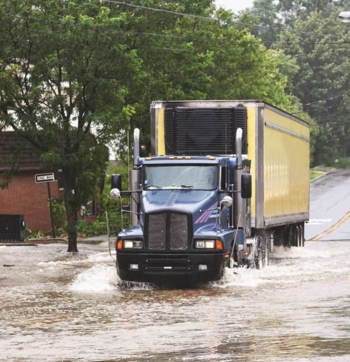 Large commercial truck navigating a flooded street after a storm demonstrating the challenges of delivering emergency supplies during severe weather events and natural disasters.