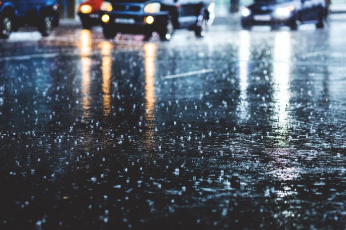 Cars driving through heavy nighttime rain on a reflective road surface depicting hazardous storm conditions that can lead to vehicle damage and insurance claims