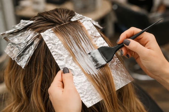 A generic colorist's hands apply highlights to a foil in a color client's hair.