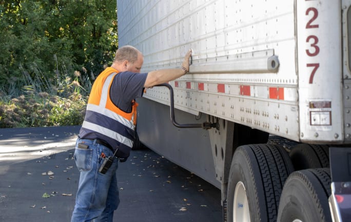 Truck driver in orange safety vest cranking landing gear on a trailer