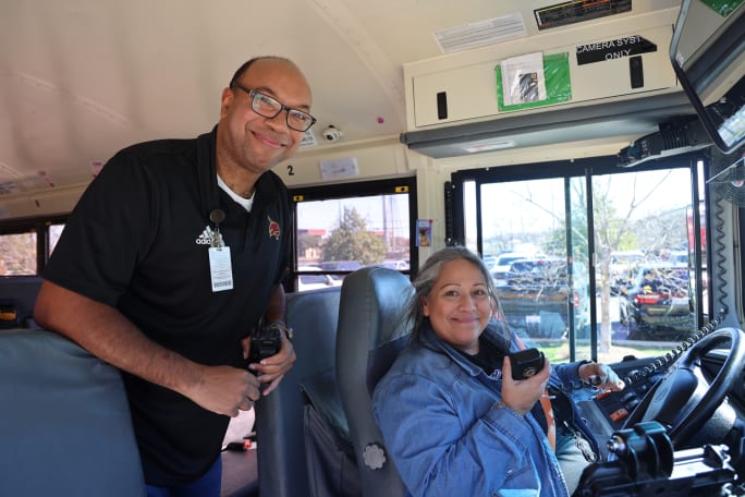 Anthony Shields stands inside a school bus next to a driver on the radio
