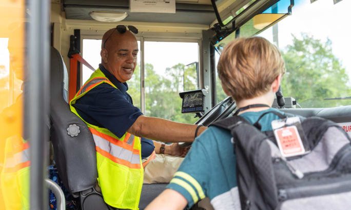 A school bus driver looks on as a student boards the school bus.