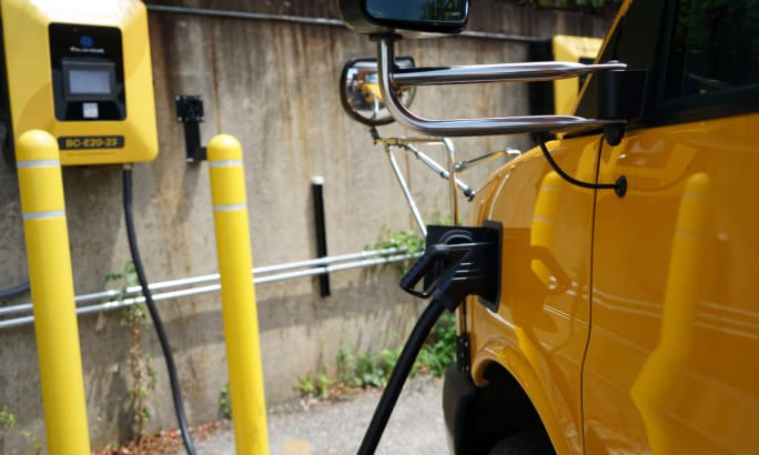 An electric school bus charges in a parking lot.