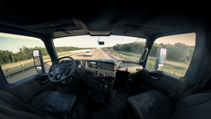 Interior of Class 8 truck cab, with no one in driver or passenger seats, looking out front and side windows from sleeper in a wide angle shot.