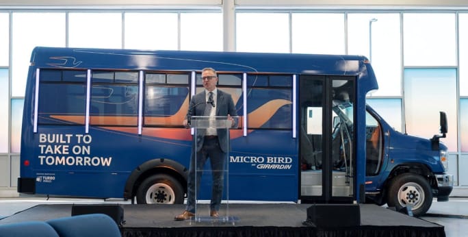 john wyskiel stands in front of a micro bird shuttle bus