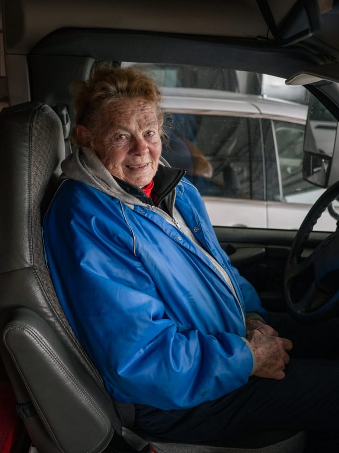 a woman in a blue jacket sits in a school bus drivers seat
