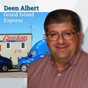 Man with glasses with Grand Island Express headquarters and trucks in the background
